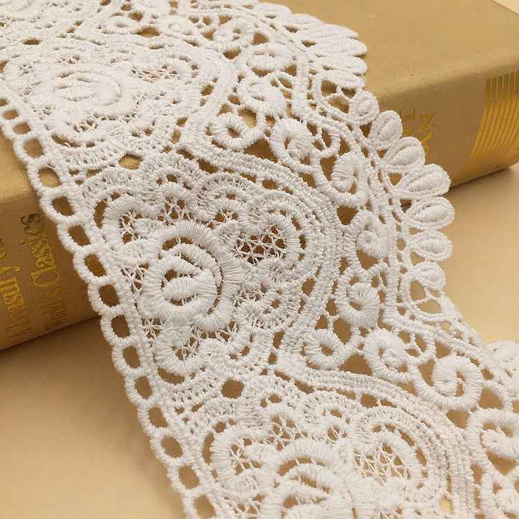 White lace trim with raised floral rosettes and cutout geometric embroidery pattern