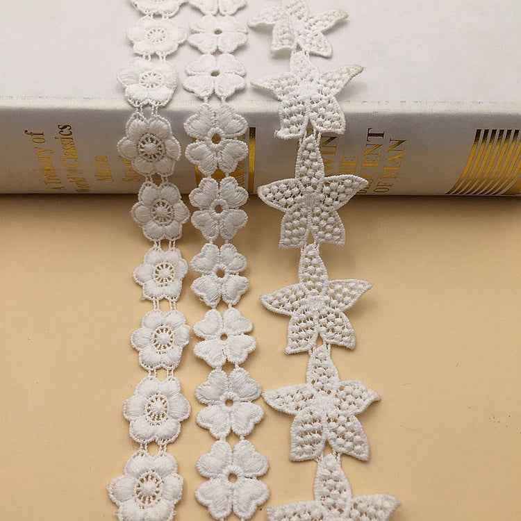 White embroidered lace trim with flowers and star-shaped motifs on a vertical strip