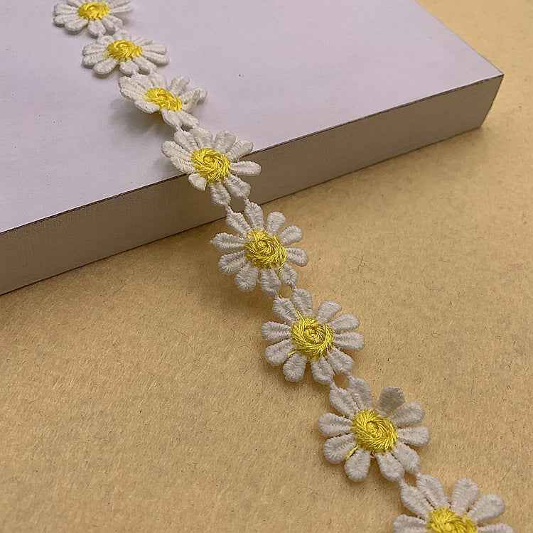 Floral daisy lace trim with white petals and bright yellow centers on a continuous border