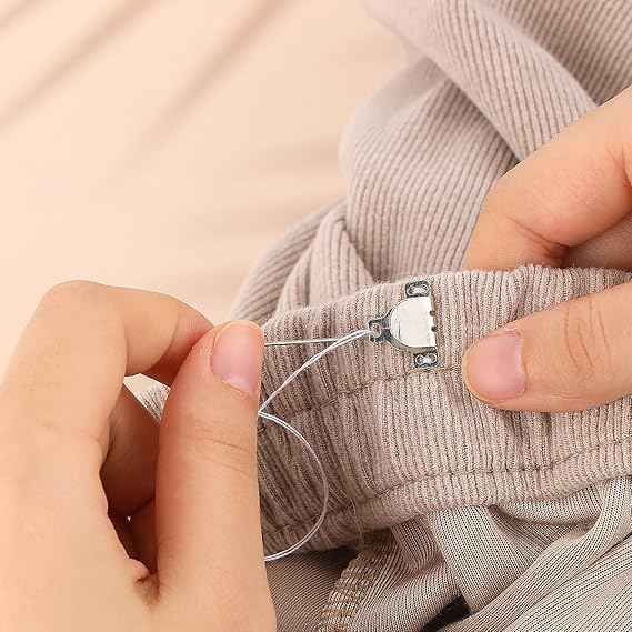 Threaded needle and hands attaching a trouser hook fastener to fabric