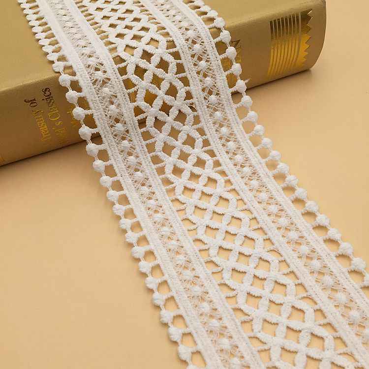White lace trim with repeating geometric embroidery and pom-pom fringe edge.