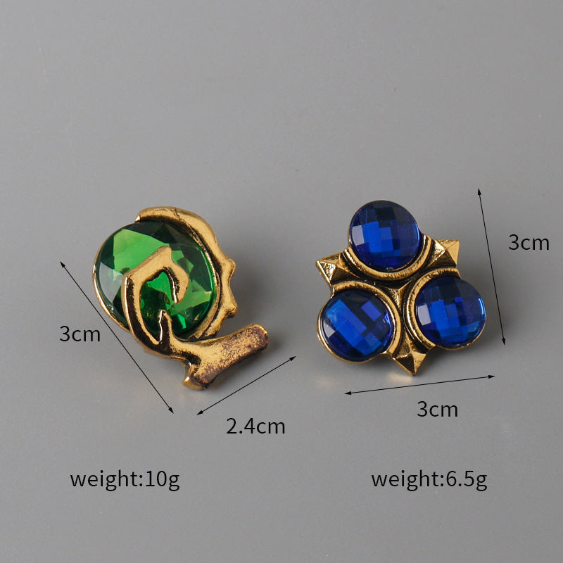 Zwei Anstecknadeln: goldfarbener Ring mit grünem Stein und dreifacher blauer Steinring