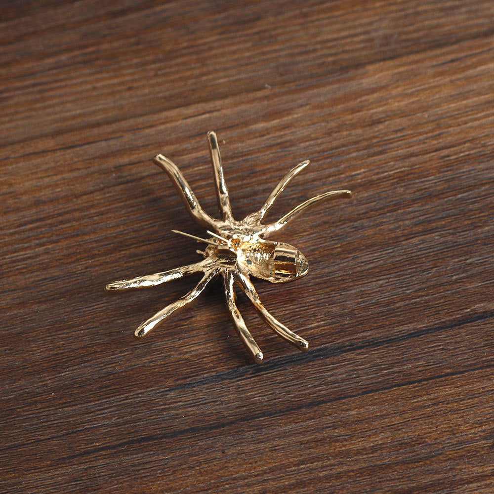 Spider brooch with gold-tone pin back, clear rhinestone web and red center accent