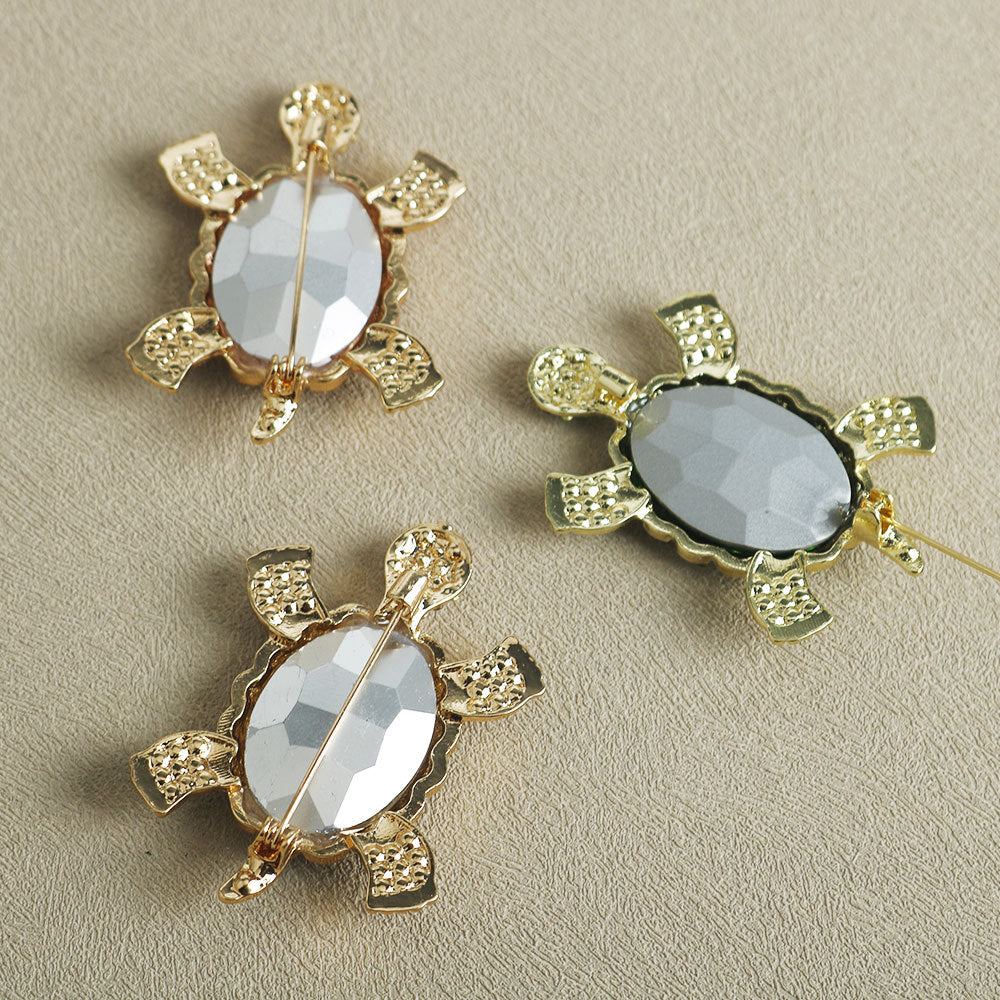 Turtle brooches set: clear oval gems in gold frames with glitter accents, pin backs visible