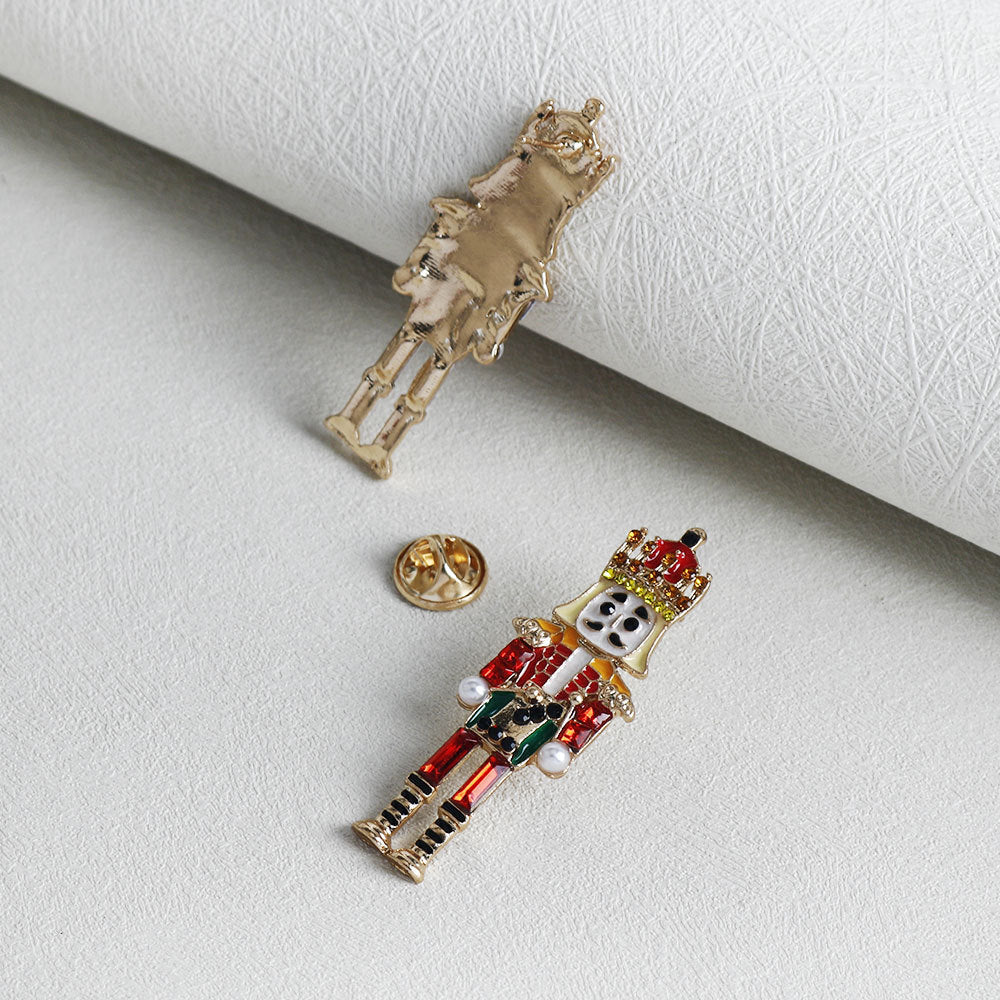 Nutcracker soldier brooch with red uniform, green belt, pearl accents, pin backing visible