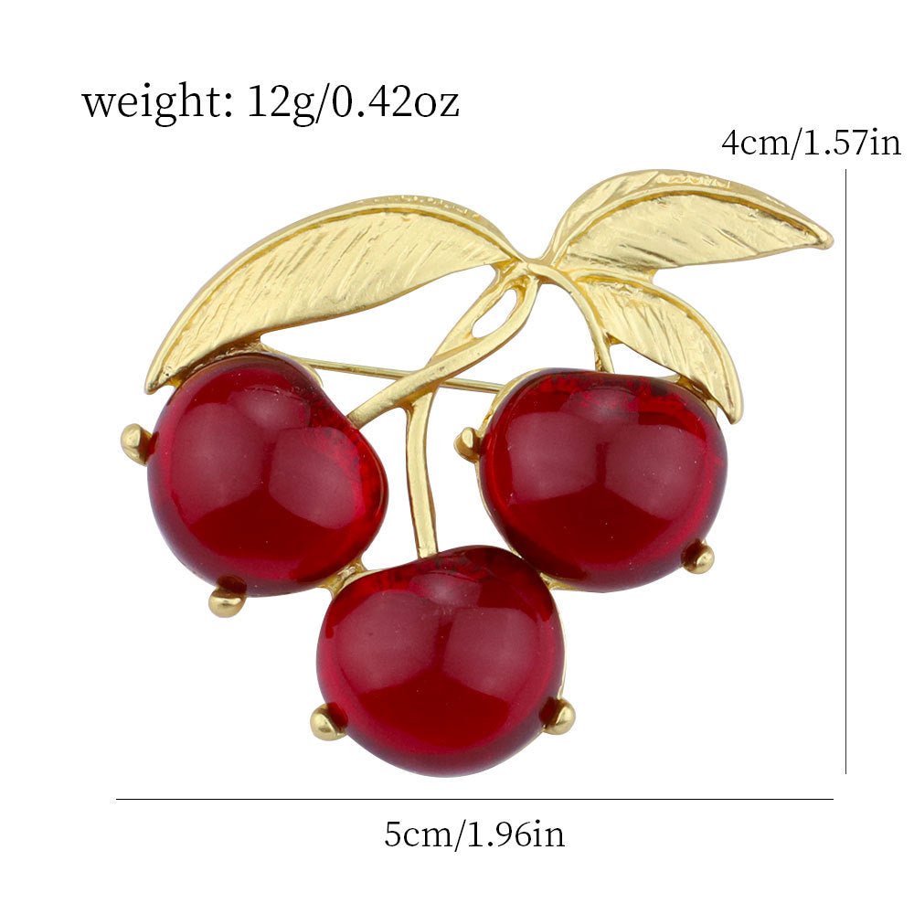 Gold-tone brooch with three red cherry jelly domes and leaf stems, pin backs visible