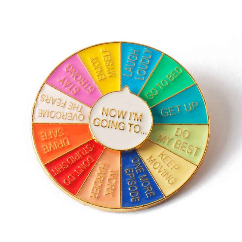 Circular spinner brooch 'NOW I'M GOING TO…' with colorful segments and gold rim