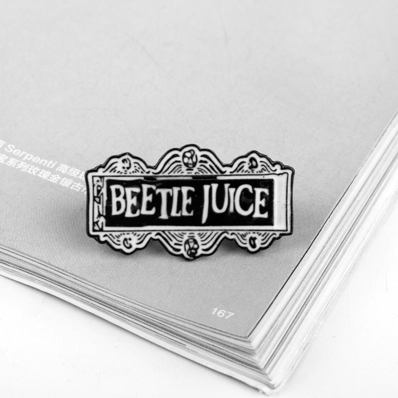 Alloy brooch “BEETLE JUICE” on backing card, decorative border and skull details