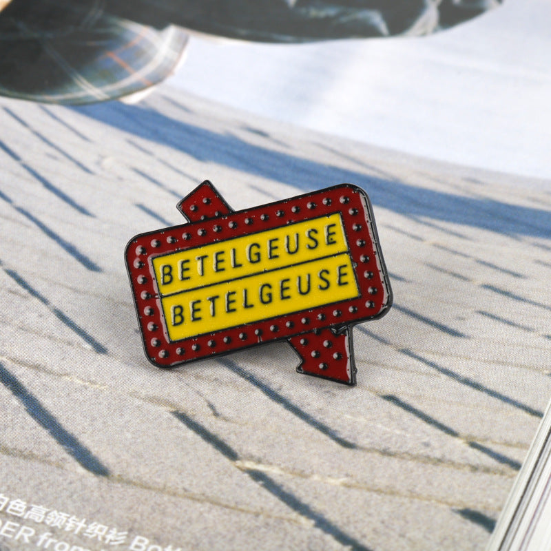 Red “BETELGEUSE” alloy brooch with studded border and white lettering