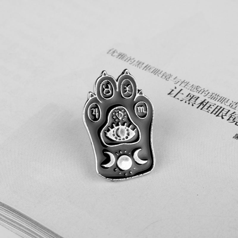 Dark enamel cat paw claw brooch with zodiac icons and moon-sun details