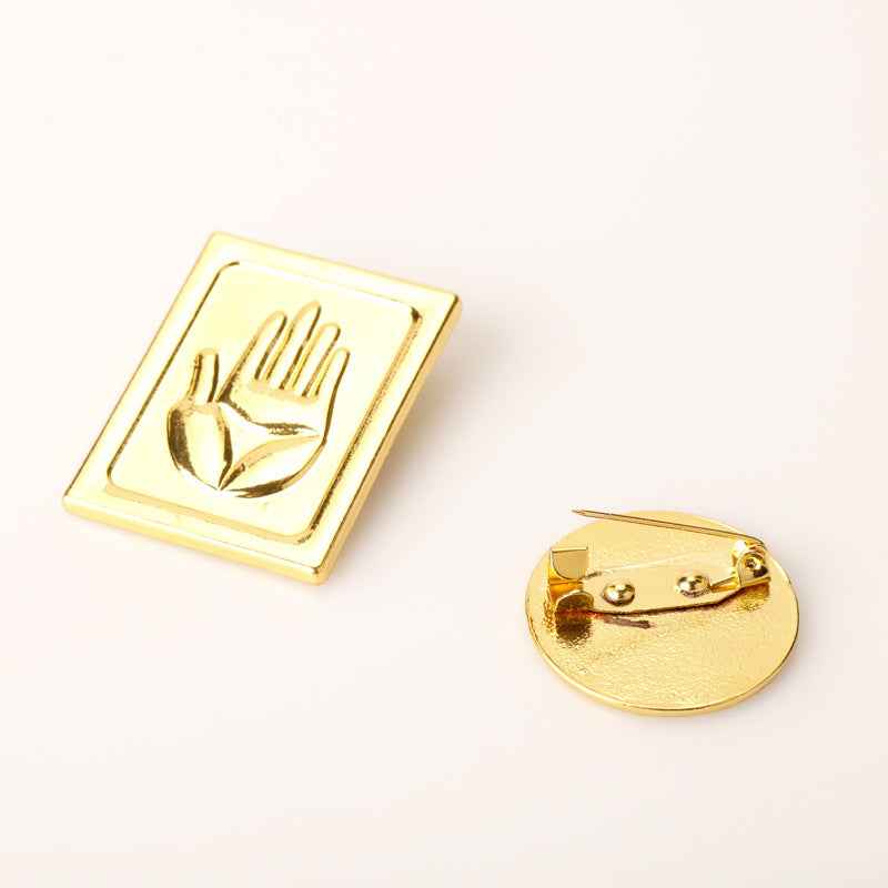 Square gold brooch with hand emblem and round gold pin back with clasp