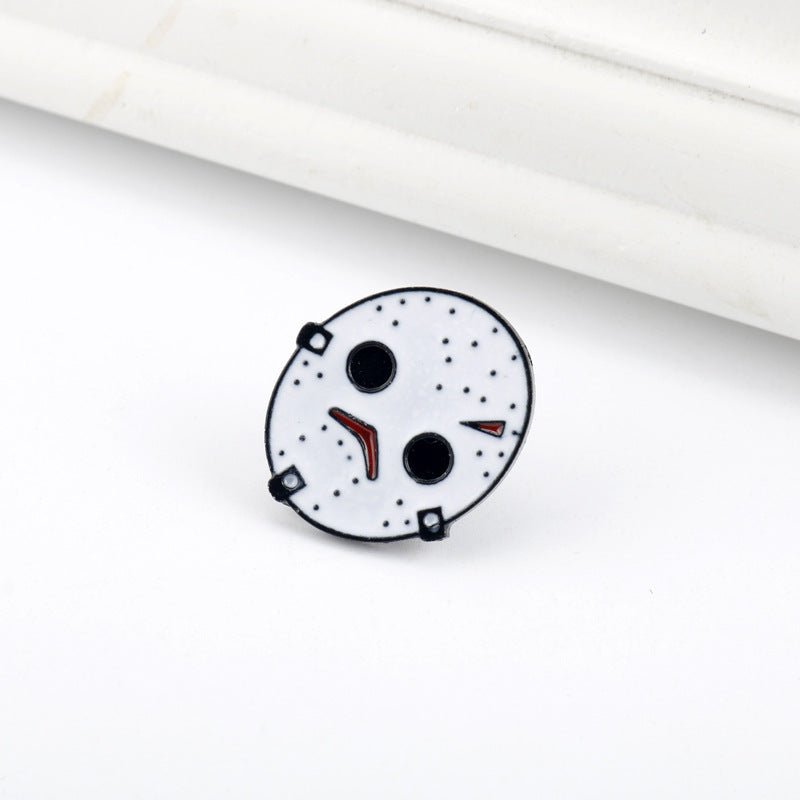 Jason-style white enamel mask pin with black eyes, red slash, and small studs