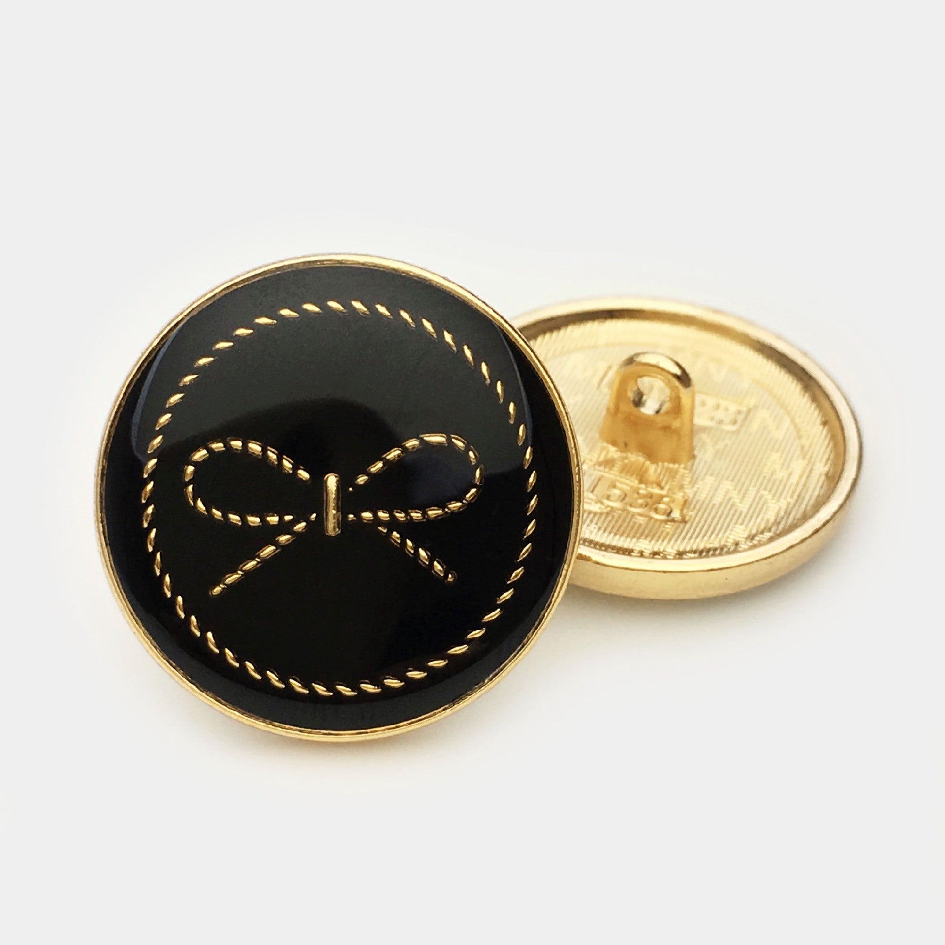 Black round bow button with gold-tone rim; reverse shows metal attachment shank