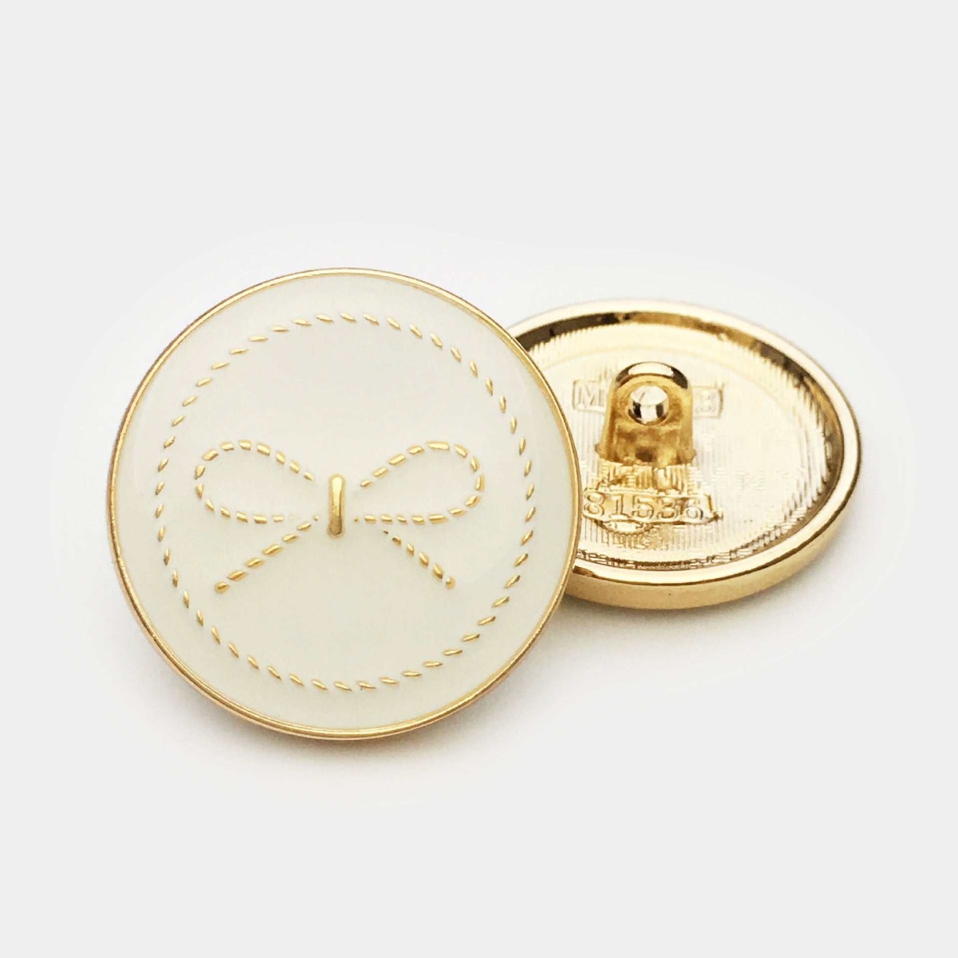 White round button with bow motif; gold-tone back and attachment shank visible
