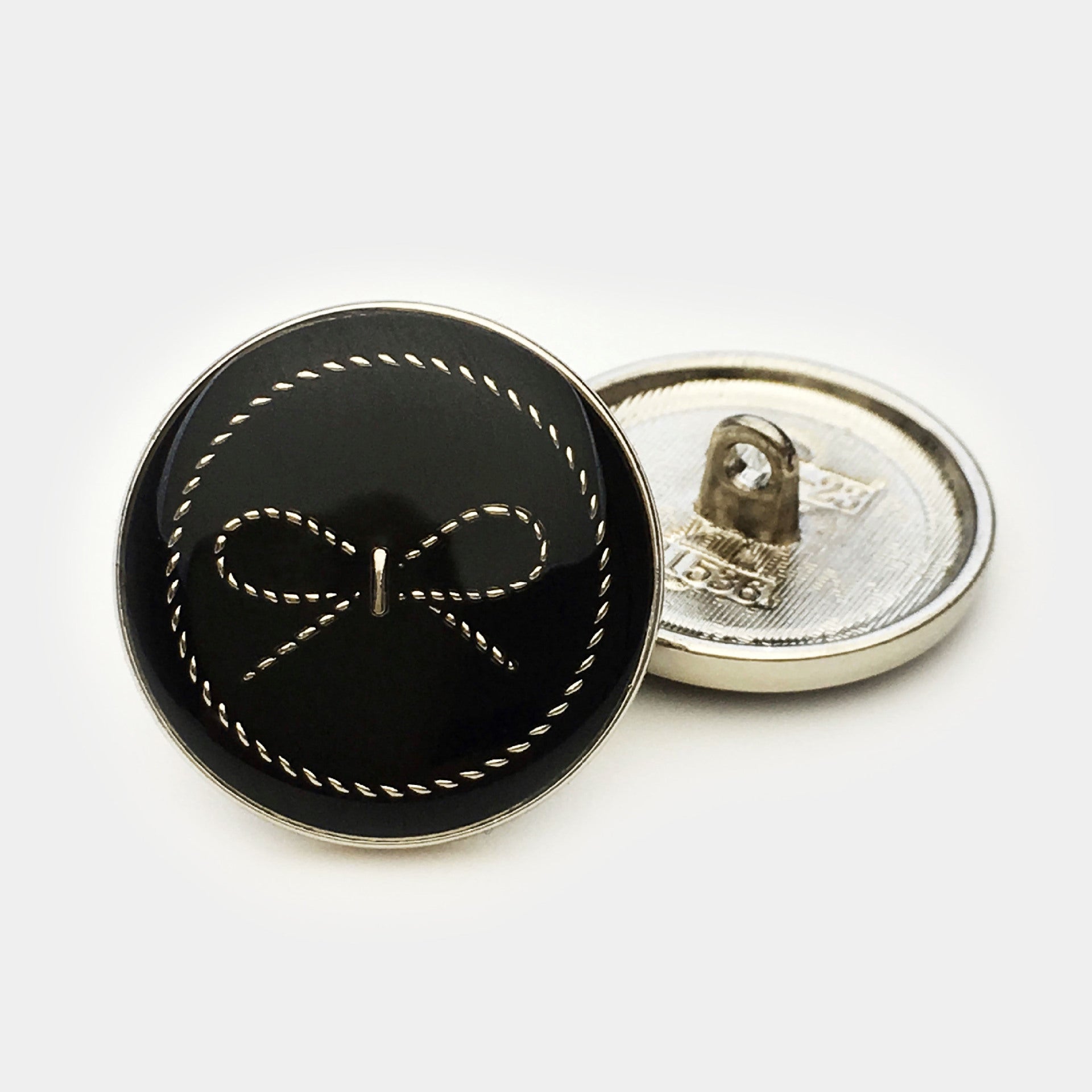 Black round bow button with stitched detail; reverse shows silver-tone metal back