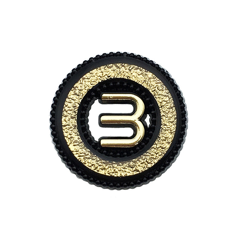 Black hollow metal button with letter M, gold textured rim, shank