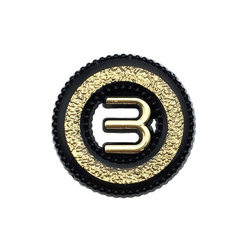 Black hollow metal button with letter M, gold textured rim, shank