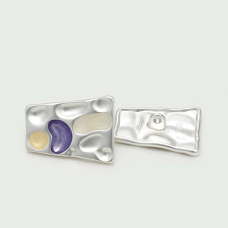 Silver tone trapezoidal metal button showing purple and pale yellow insets; back visible