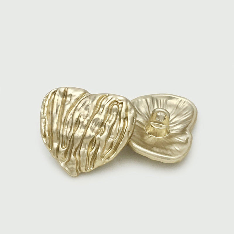 Gold heart-shaped metal button with vertical stripes and visible back loop