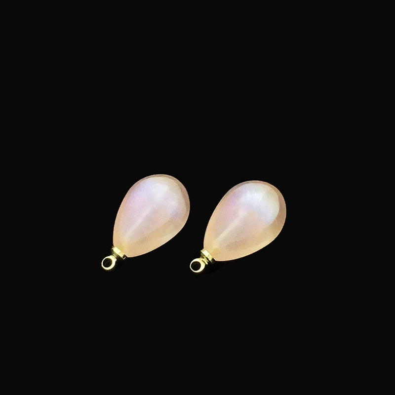 Two iridescent teardrop buttons in pale pink/cream with metal loops