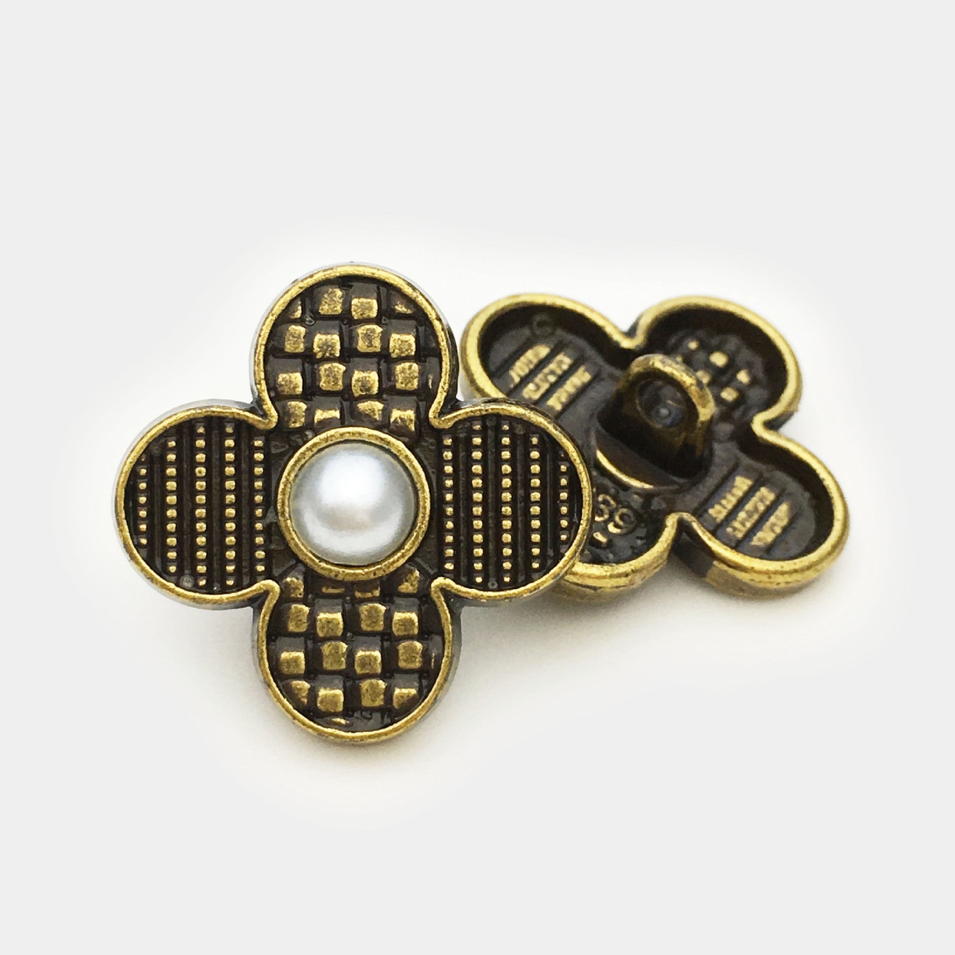 Close-up: gold-tone four-leaf clover metal button with faux pearl center and black enamel