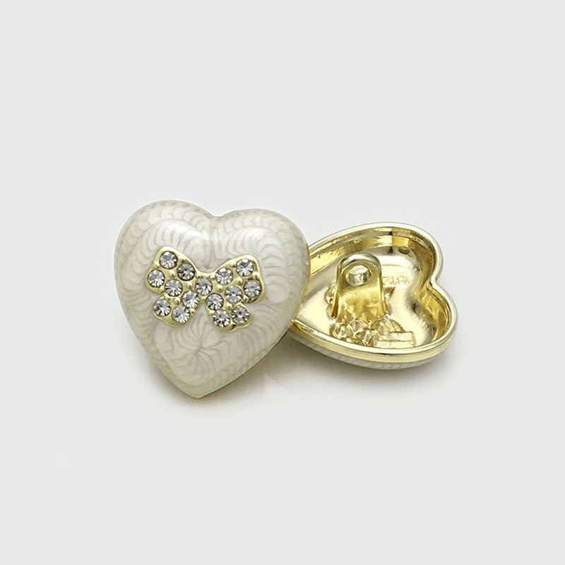 White heart-shaped metal button with crystal bow front and gold back