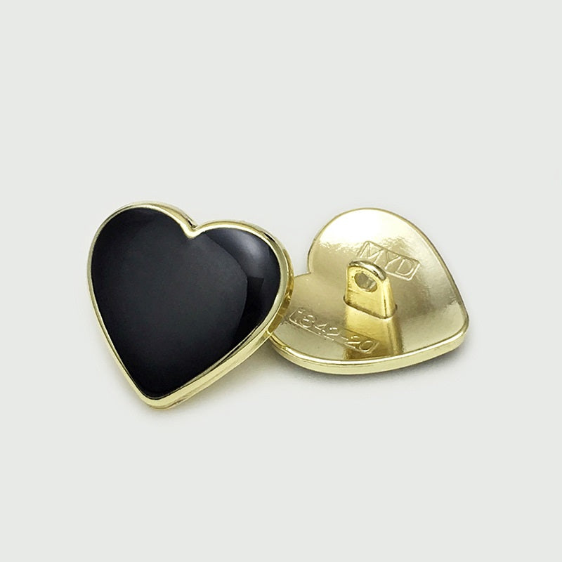 Heart button with black face; gold-tone rim and visible metal shank on back.