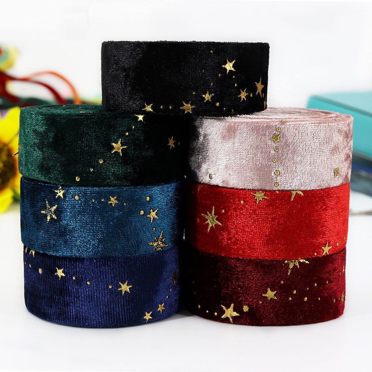 Stacked velvet ribbon rolls in dark green, blue, pink and red with gold star embroidery