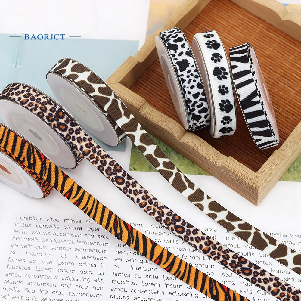 Assorted animal print ribbon rolls on a wooden holder: giraffe, leopard, zebra, paw, cow