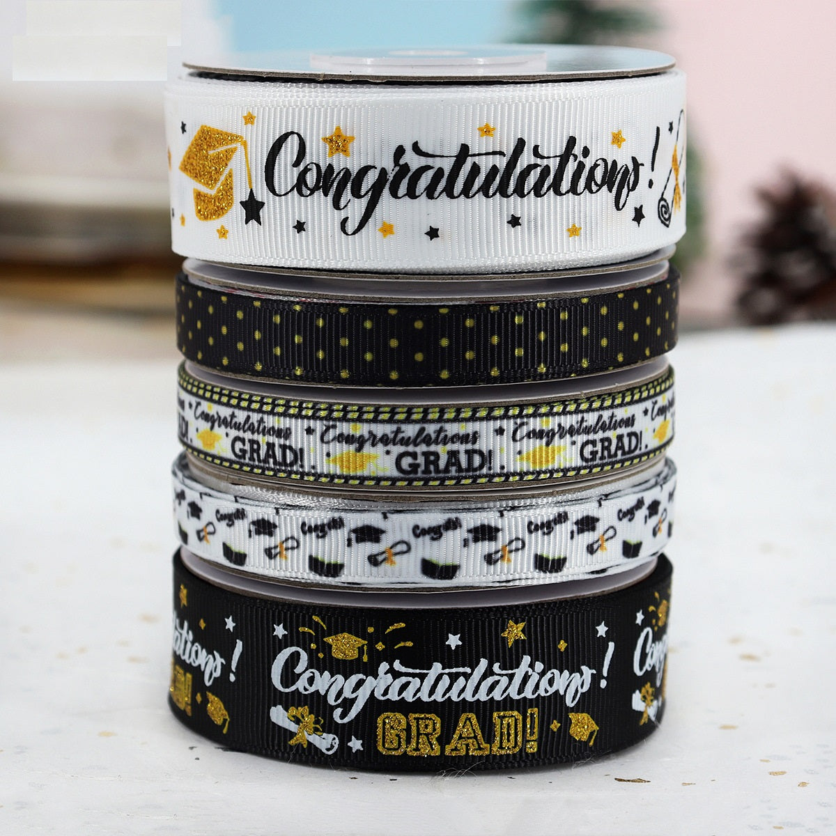 Stack of graduation ribbon rolls: white, black, and gold “Congratulations! GRAD!” print