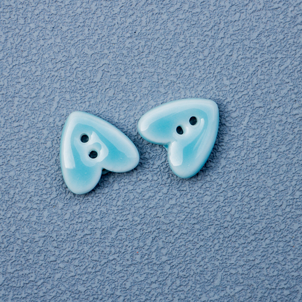 Light blue heart-shaped 2-hole ceramic buttons pair, two visible stitching holes