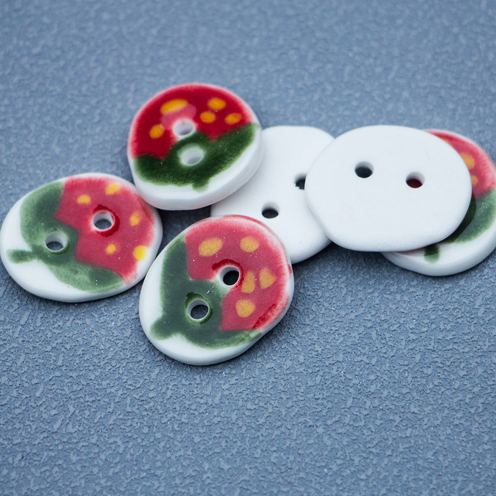 Oval ceramic buttons with red-green strawberry pattern, showing two holes; one plain button
