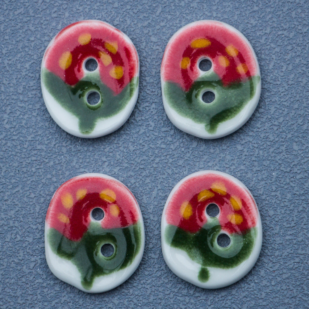 Two oval ceramic buttons with red-green strawberry print and yellow dots; two holes