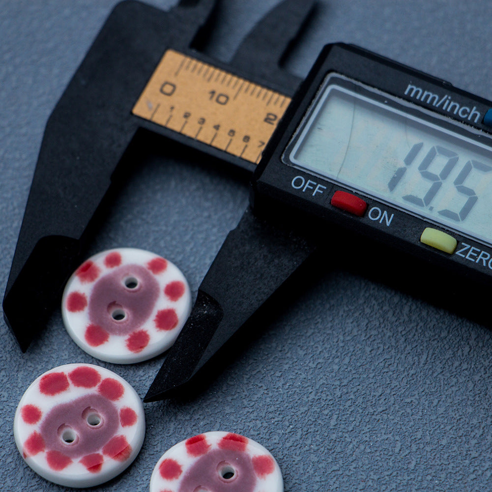 Round 2-hole ceramic button with red-dotted pig design, shown next to caliper