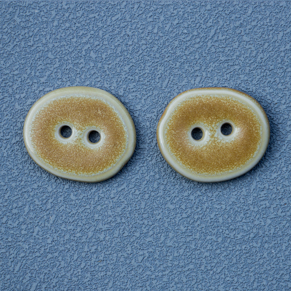 Sand-colored irregular oval ceramic button, 2-hole, close-up view