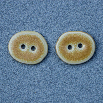 Sand-colored irregular oval ceramic button, 2-hole, close-up view
