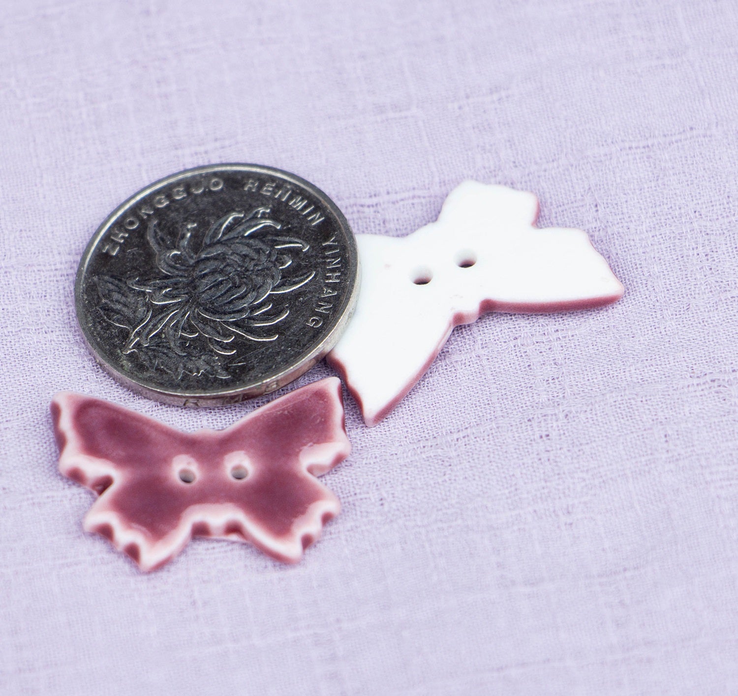 24mm butterfly ceramic button in purple-red glaze, 2 holes; beside a coin.