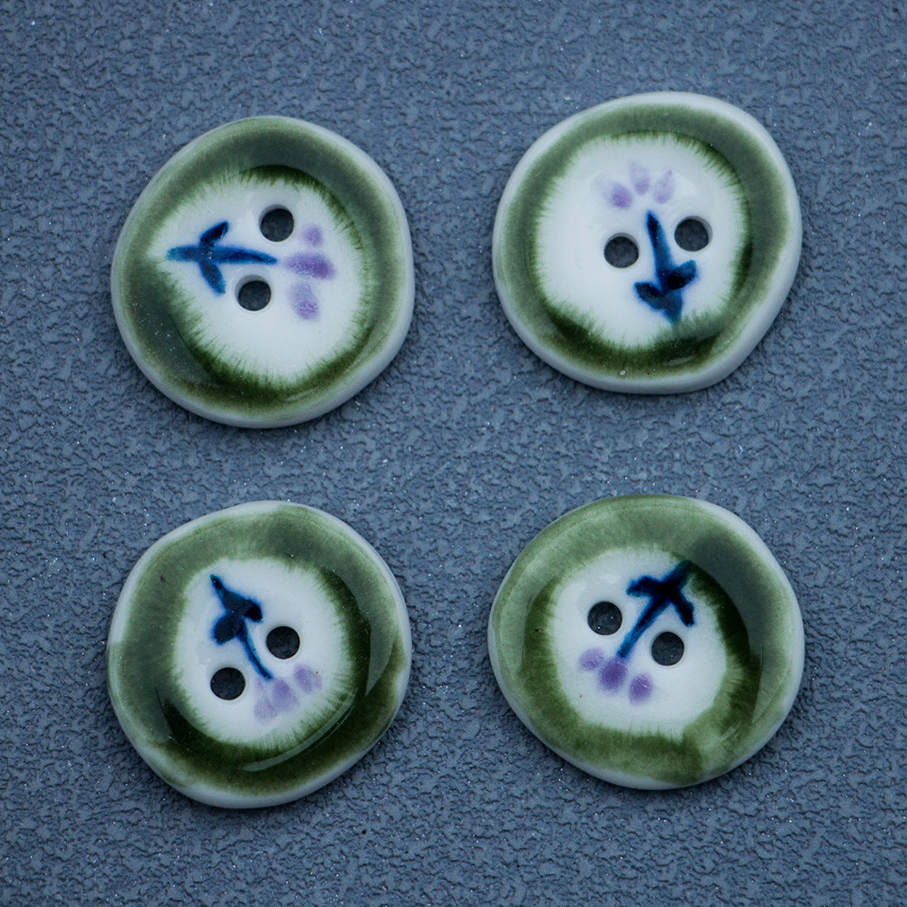 Four 20mm irregular round ceramic buttons, green rim, hand-painted blue/purple motif