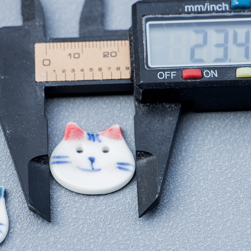 Cat ceramic button close-up, red/pink ears and blue face details on white