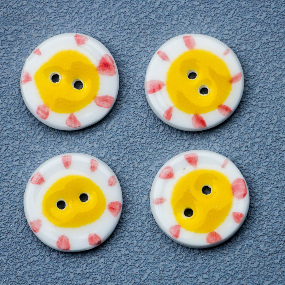 Four round ceramic buttons with two holes, yellow sun pattern and pink accents