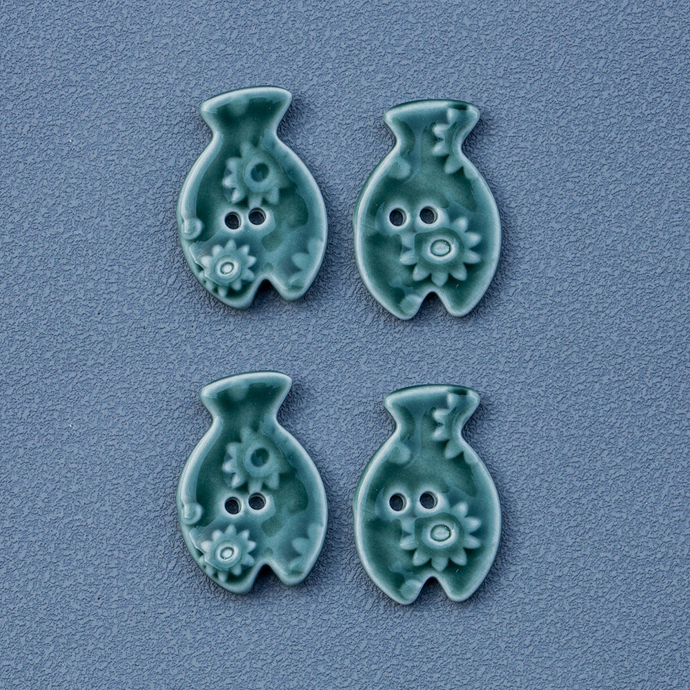 Set of four green fish-shaped 2-hole ceramic buttons with embossed flower motifs.