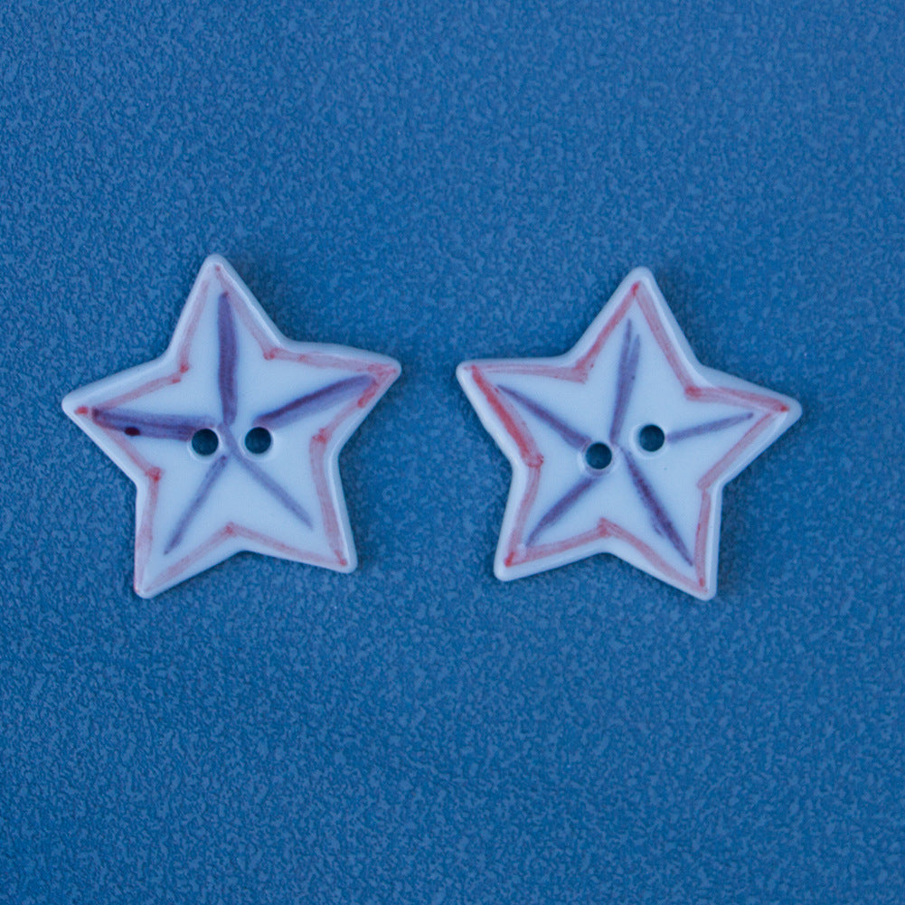 Two star-shaped ceramic buttons, white with red/purple matchstick pattern, two holes