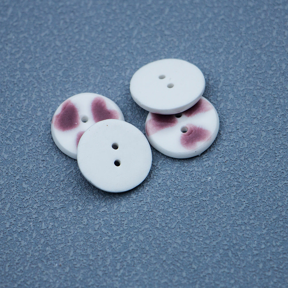 Set of round two-hole ceramic buttons with purple-red heart pattern on white
