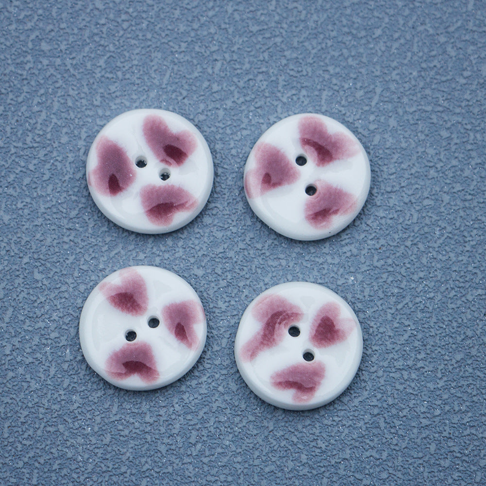 Four round two-hole ceramic buttons with hand-painted purple hearts on white