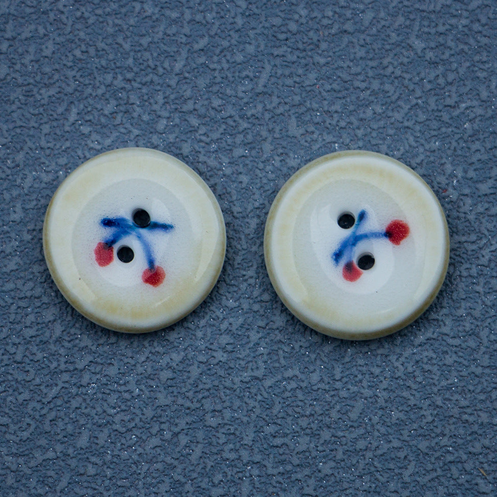Ceramic buttons with hand-painted cherry design; cream face, blue and red motif, brown edge, 2 holes.