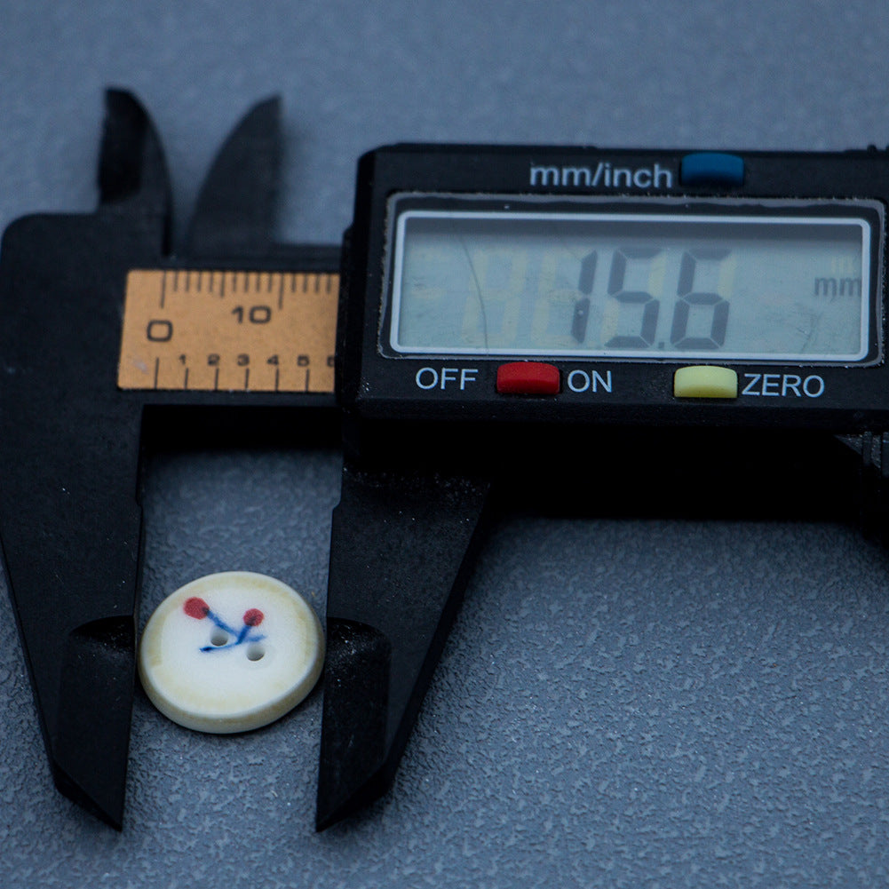 Ceramic button with cherry motif, cream face and brown rim; measured ~16 mm, 2 holes.