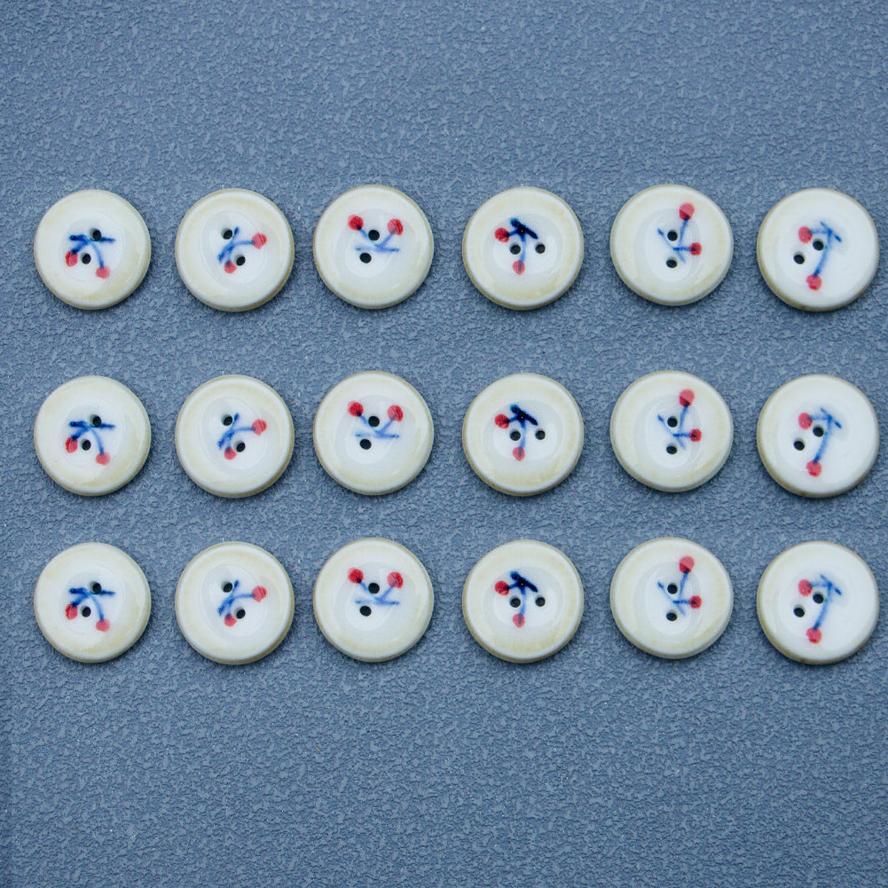 Ceramic buttons with cherry pattern; cream faces, brown rims, blue stems and red berries, 2 holes.