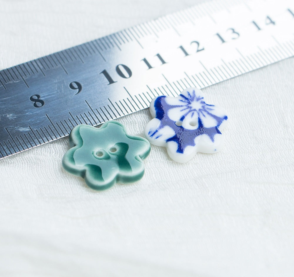 Small ceramic flower buttons with two holes in green and blue; size shown by ruler