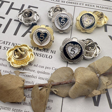 Heart-shaped number 5 metal brooches in gold and silver tones with dark blue centers
