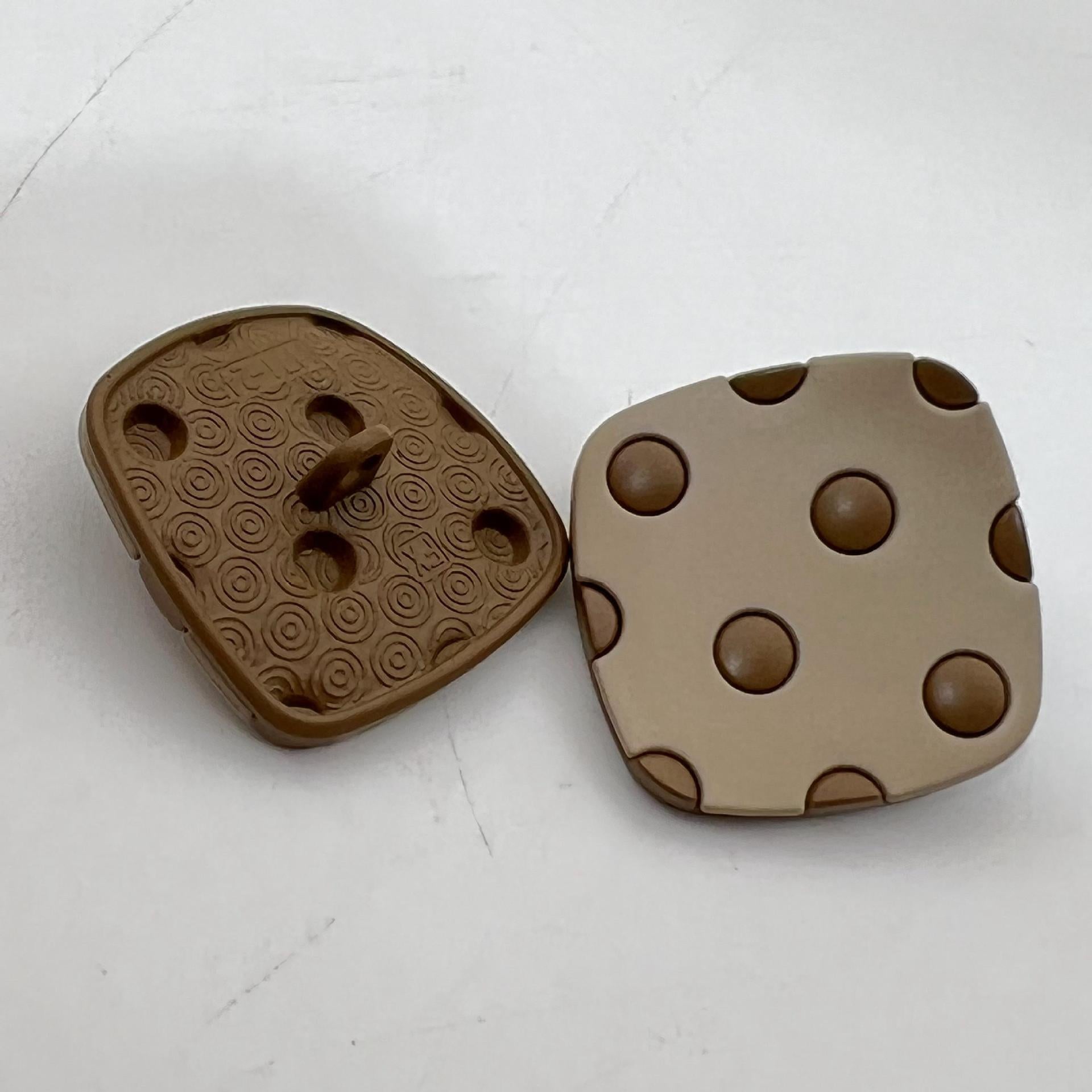 Curved square metal shank buttons with four studs; warm brown and light tan tones
